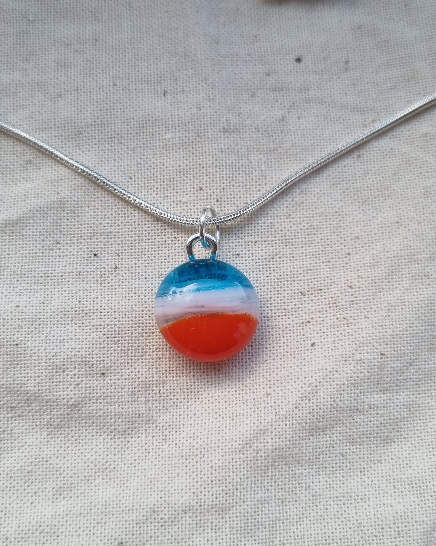 Blue, white and orange handmade glass pebble pendant.